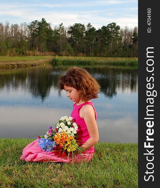 A pretty little girl is sitting on the grass holding flowers on the lake background. A pretty little girl is sitting on the grass holding flowers on the lake background