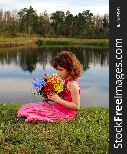 A cute girl in pink outfit is holding flowers on lake background. A cute girl in pink outfit is holding flowers on lake background