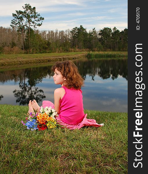 A cute girl in pink outfit is sitting at the lake with flowers bouquet next to her. A cute girl in pink outfit is sitting at the lake with flowers bouquet next to her