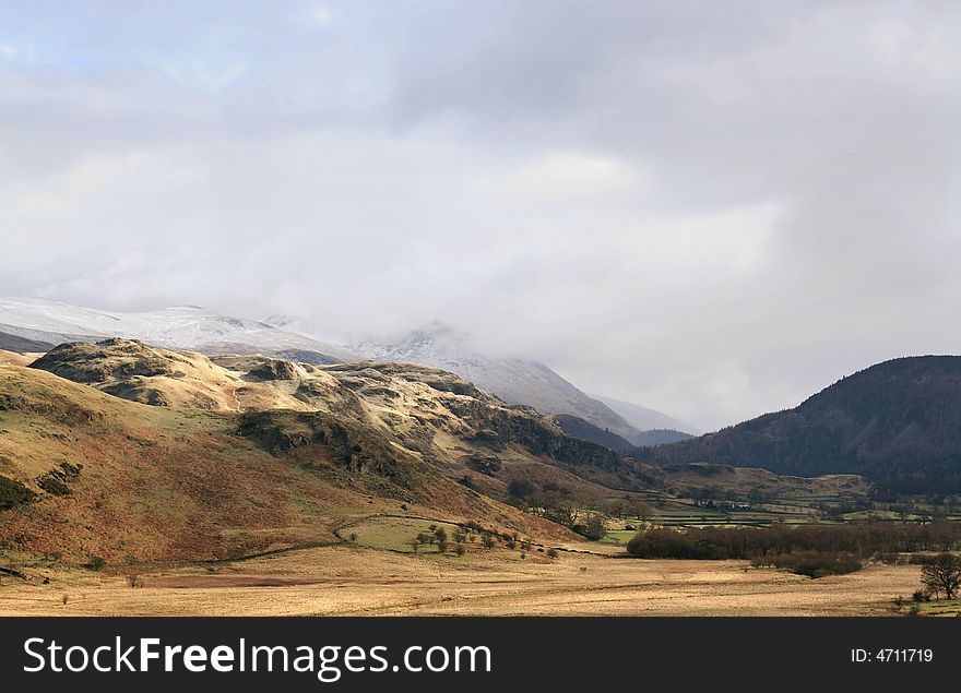 A view of Fells in the English Lake District with a cloud and snow topped Hellvelyn in the distance. A view of Fells in the English Lake District with a cloud and snow topped Hellvelyn in the distance