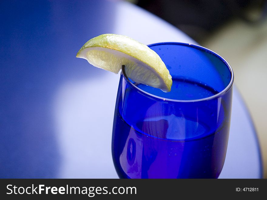 A lemon slice on a blue crystal water glass against a blue table. A lemon slice on a blue crystal water glass against a blue table