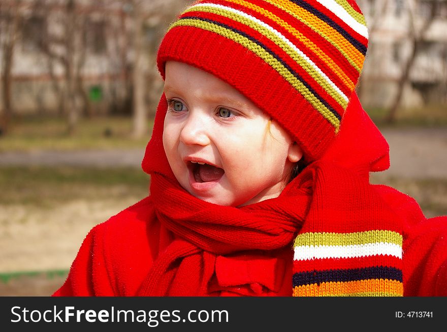 The little girl in a bright cap and a scarf shouts. The little girl in a bright cap and a scarf shouts