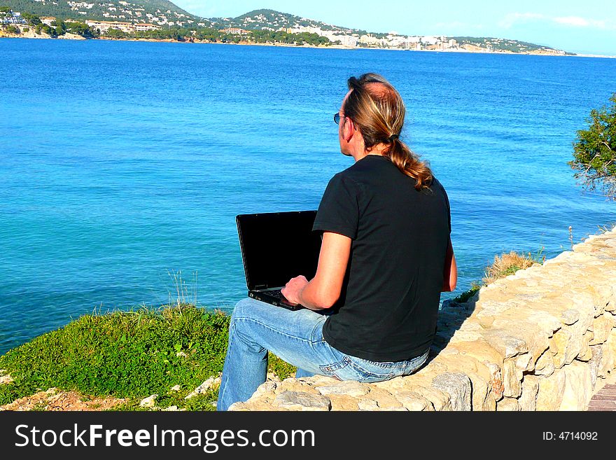 A Man working on a laptop computer by the sea. A Man working on a laptop computer by the sea