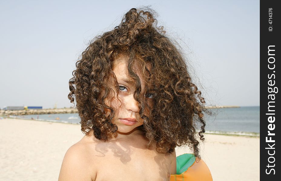 Little curly girl on the beach ready to swim in the sea.