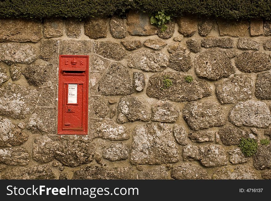 Traditional British red postbox in English village wall (Chagford, Devon), with collection times removed from front