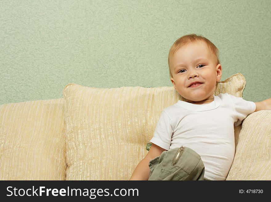 The cheerful little boy sits and on a sofa and smiles
