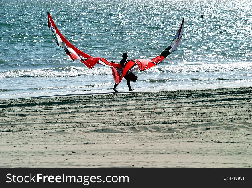 Kitesurfer walking down a beach after exhausting workout. Kitesurfer walking down a beach after exhausting workout.