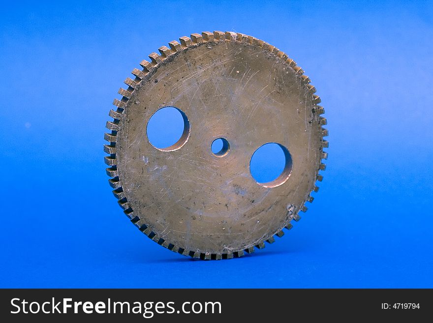 Old perforated and scratched cogwheel against the blue background.