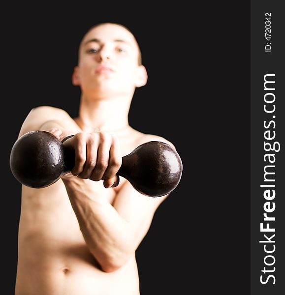 Young man with dumbbell. Focus on dumbbell, isolated on black.