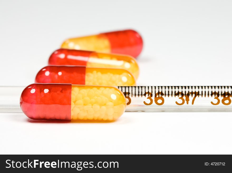 Antibiotic pills and a medical glass thermometer on white background. Antibiotic pills and a medical glass thermometer on white background