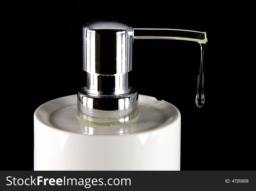 Liquid soap dripping from dispenser, on dark background