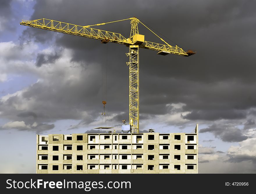 Hoisting crane lifting a concrete slab on a house being built, on the background of gloomy thunder clouds. Hoisting crane lifting a concrete slab on a house being built, on the background of gloomy thunder clouds