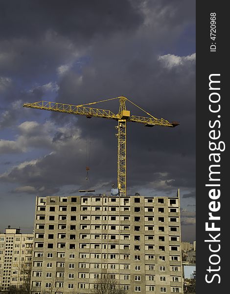 Hoisting crane lifting a concrete slab on a house being built, on the background of gloomy thunder clouds. Hoisting crane lifting a concrete slab on a house being built, on the background of gloomy thunder clouds