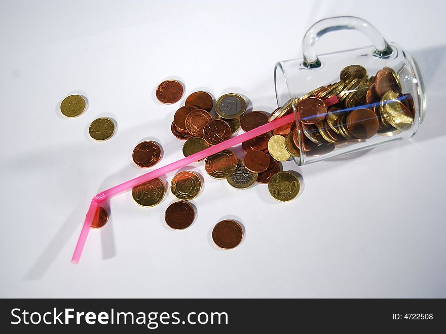 A glass filled with change and a straw falls down and spills the money. A glass filled with change and a straw falls down and spills the money