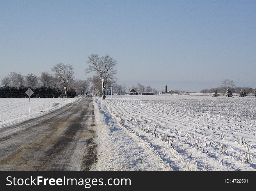 Country road after a snow storm in the midwest. Corn fields and farms in the distance. Country road after a snow storm in the midwest. Corn fields and farms in the distance.