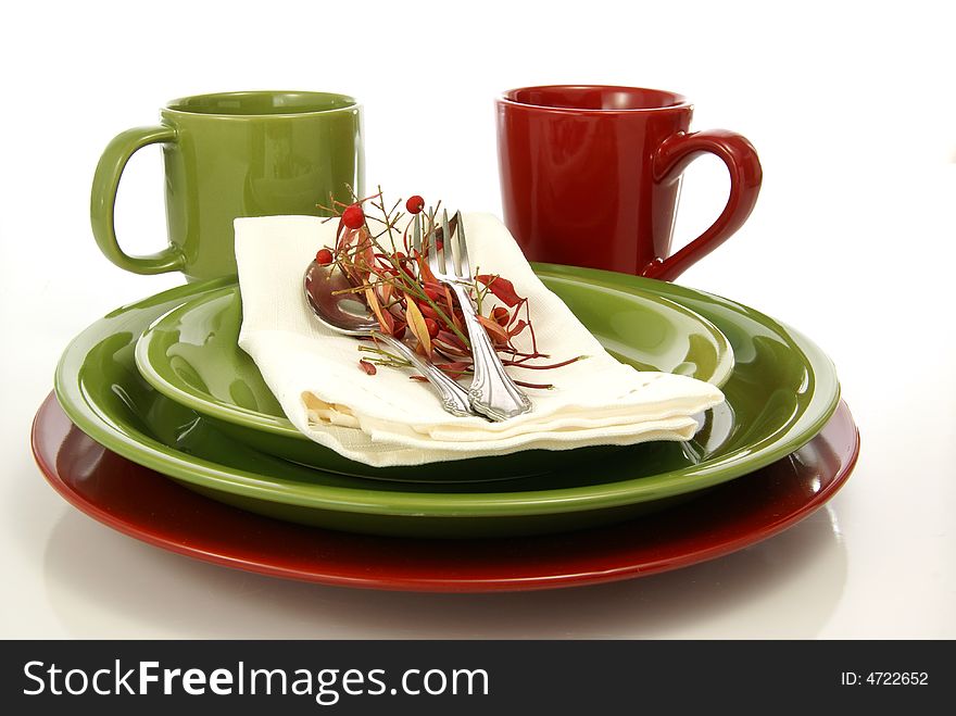 Green and red tableware setting with plates, coffee mugs, and cloth napkin. Green and red tableware setting with plates, coffee mugs, and cloth napkin.