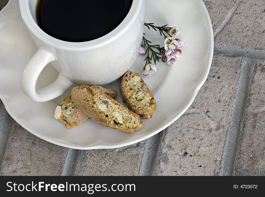 Cup of coffee with biscotti and small flowers on a brick background. Cup of coffee with biscotti and small flowers on a brick background.