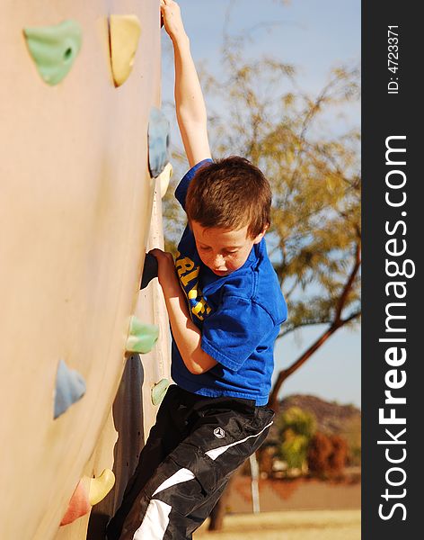 Young boy climbs rock wall at playground. Young boy climbs rock wall at playground.