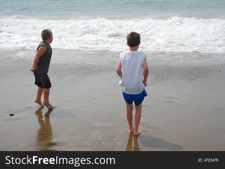 Two barefooted boys face the ocean, waiting to race the cold waves ashore. One boy is on his toes in expectation. Two barefooted boys face the ocean, waiting to race the cold waves ashore. One boy is on his toes in expectation.