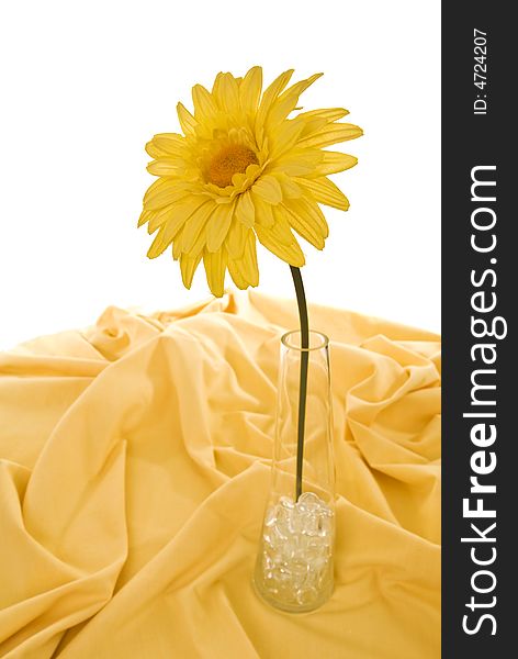 Cloth sunflower in glass vase with glass pebbles on yellow tablecloth, isolated on white.