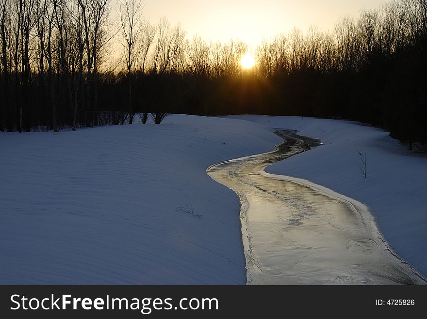 The setting sun lights up a winding creek and reflects off its icy surface. The setting sun lights up a winding creek and reflects off its icy surface
