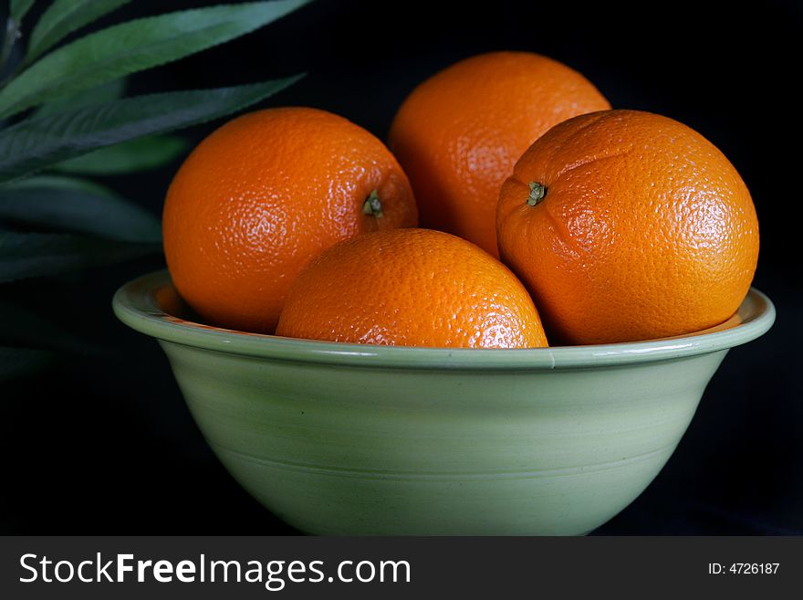 A green bowl holds several healthy oranges. A green bowl holds several healthy oranges.