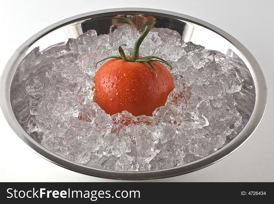 Bright red tomato resting in metal bowl of ice isolated on white. Bright red tomato resting in metal bowl of ice isolated on white