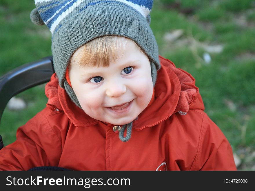 The little boy smiles on a background of a green lawn in the spring. The little boy smiles on a background of a green lawn in the spring