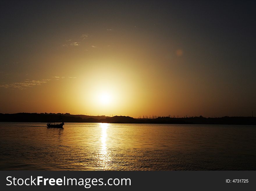 Beautiful sun low upon the river nile in egypt on a nice clear day. Sun reflecting on ripply water with a small boat gently cruising along. Beautiful sun low upon the river nile in egypt on a nice clear day. Sun reflecting on ripply water with a small boat gently cruising along.