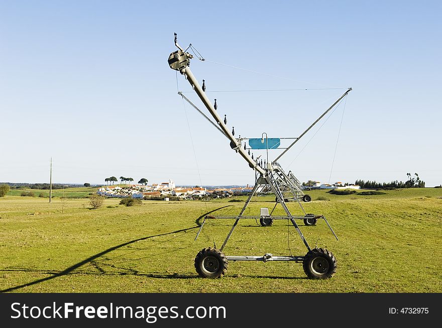 Resting irrigation pivot in a green grass field near a small village. Alentejo, Portugal