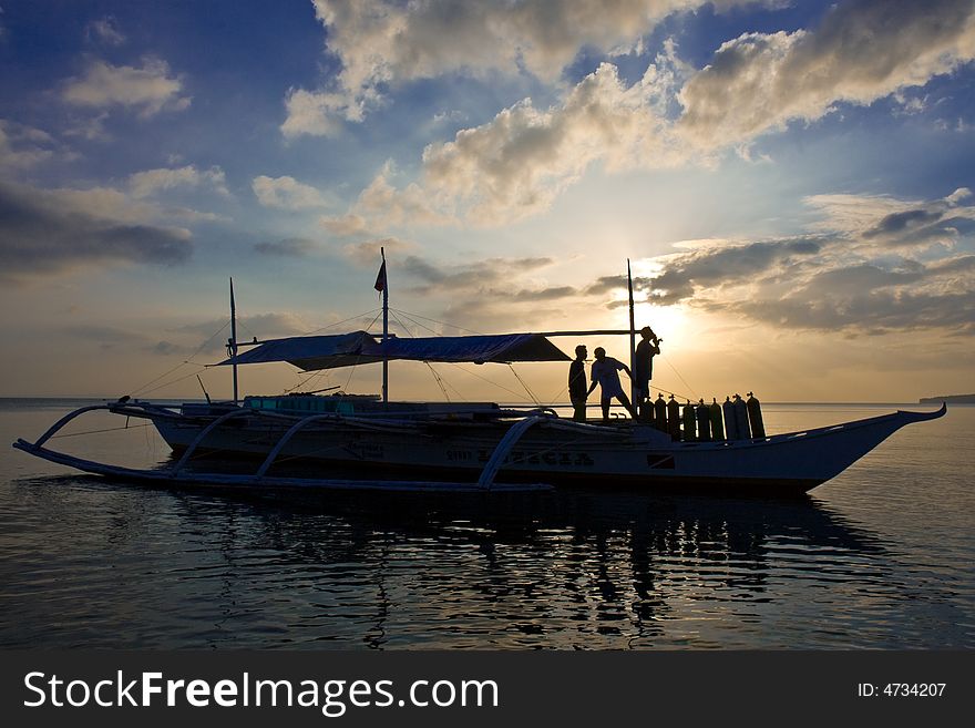 Unloading scuba tanks from a banca boat at sunset. Unloading scuba tanks from a banca boat at sunset