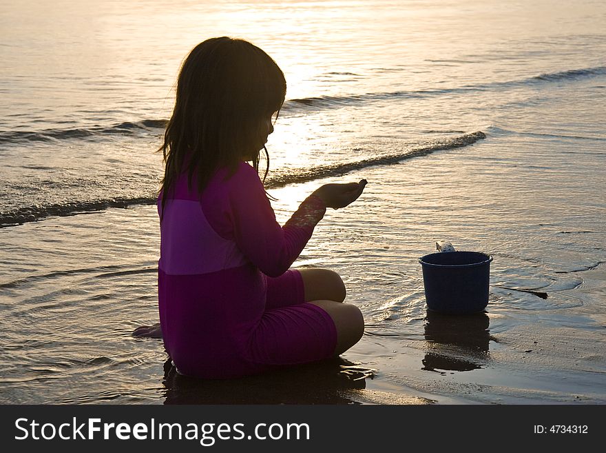 Girl playing with the sand on the beach at sunset. Girl playing with the sand on the beach at sunset