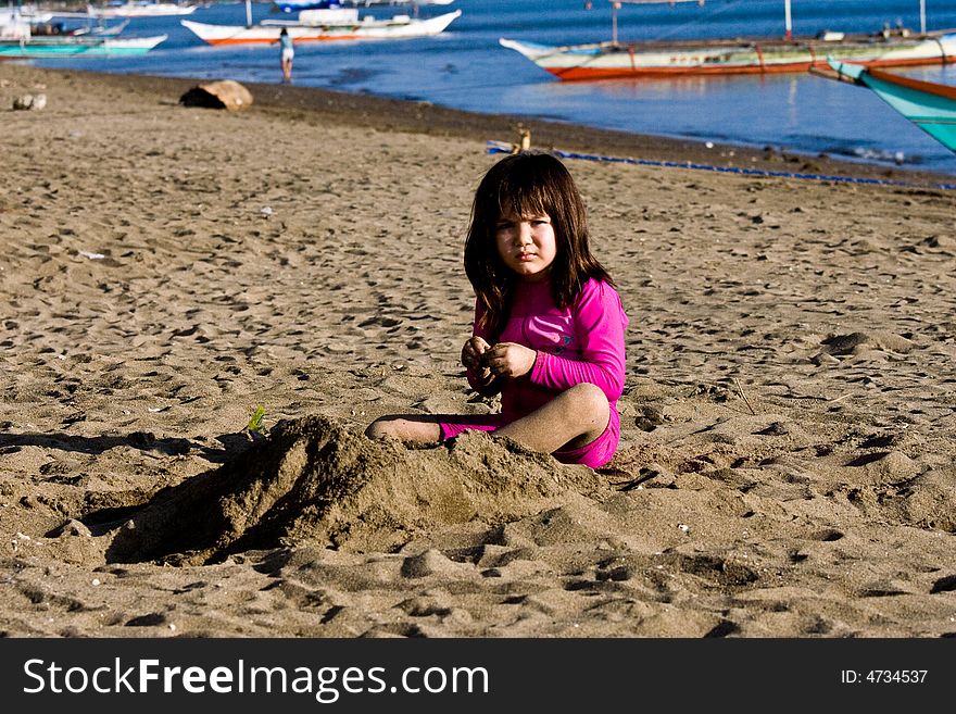 Girl playing with sand on the beach with banca boats in the background