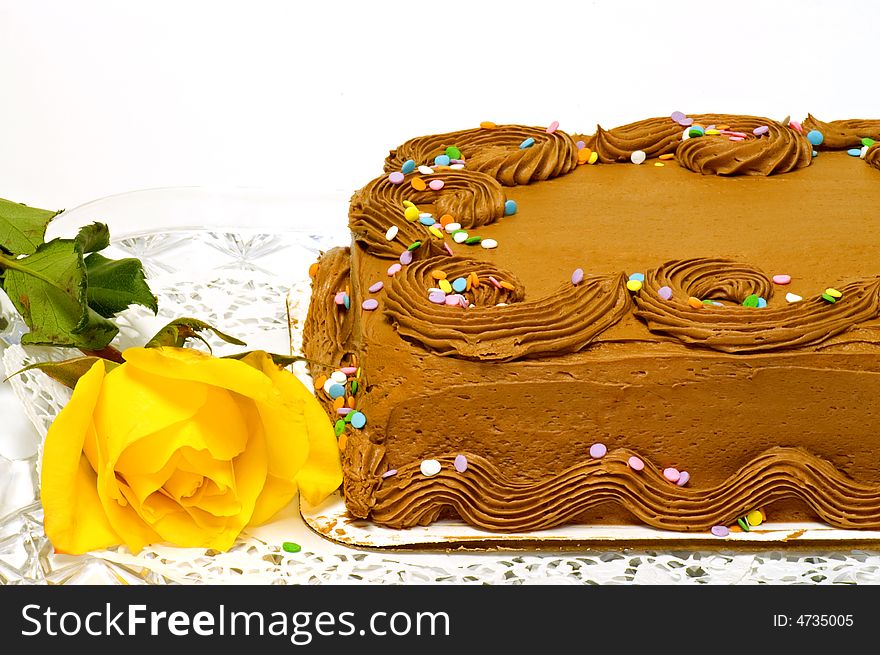 A close up view of the decorative frosting on the corner of a chocolate cake with a bright yellow rose. A close up view of the decorative frosting on the corner of a chocolate cake with a bright yellow rose.