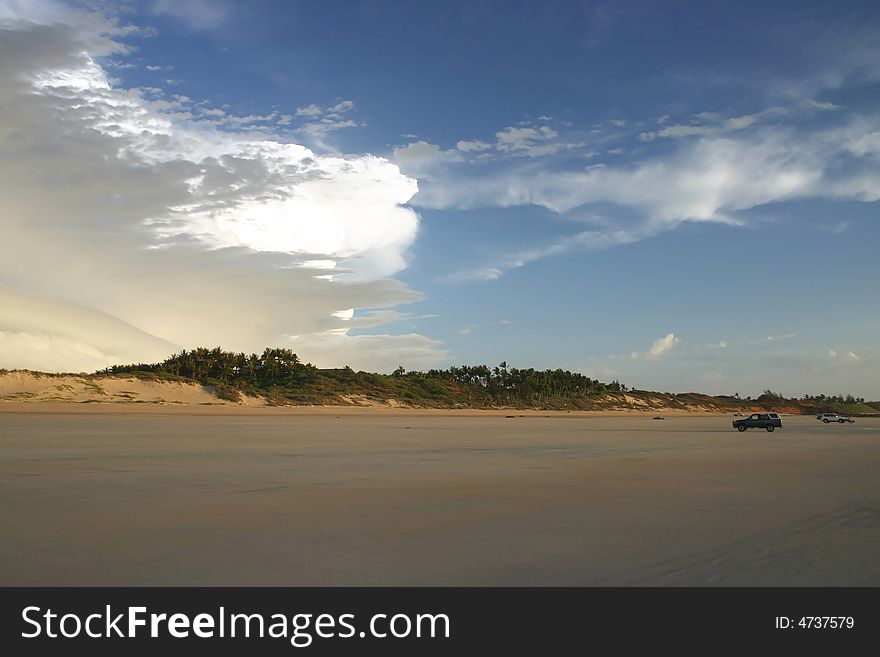 Two cars parked on a beautiful sandy beach with dramatic clouds on a blue sky. Australia. Two cars parked on a beautiful sandy beach with dramatic clouds on a blue sky. Australia.