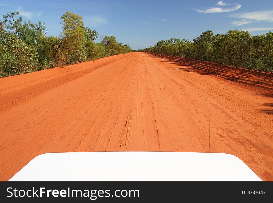 Red Australian rural road with blue sky. Perspective from the car hood. Copy space. Red Australian rural road with blue sky. Perspective from the car hood. Copy space.