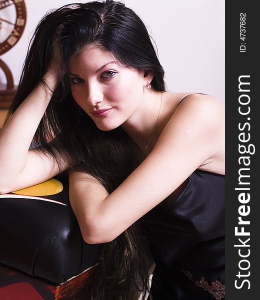 Young woman wearing a black lingerie top resting her body against a leather and wood stool. Young woman wearing a black lingerie top resting her body against a leather and wood stool