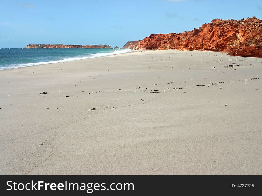 Blue clear sky over the red rocks on a long sandy beach. Australian. Blue clear sky over the red rocks on a long sandy beach. Australian