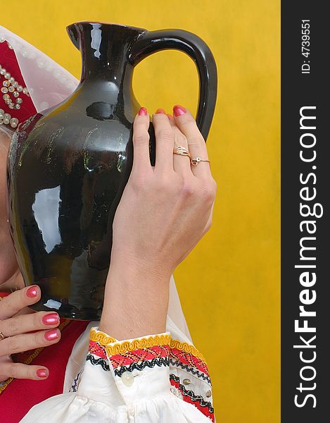 Close-up. Woman in a folk russian dress holds a jug on yellow background