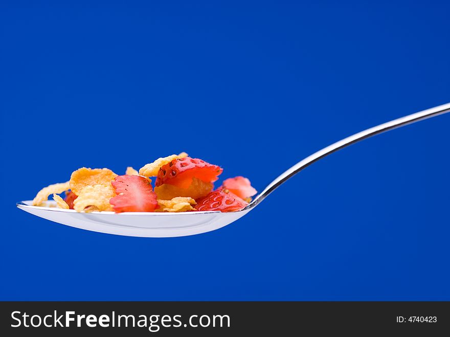 Closeup of cereal with strawberries on a spoon on a stricking blue background