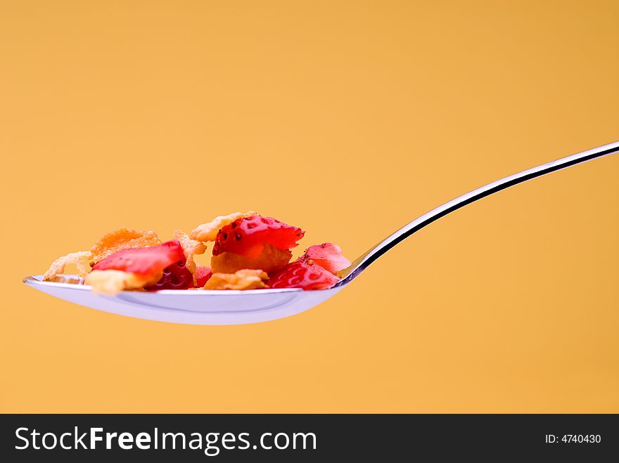 Closeup of cereal with strawberries on a spoon on a stricking yellow background