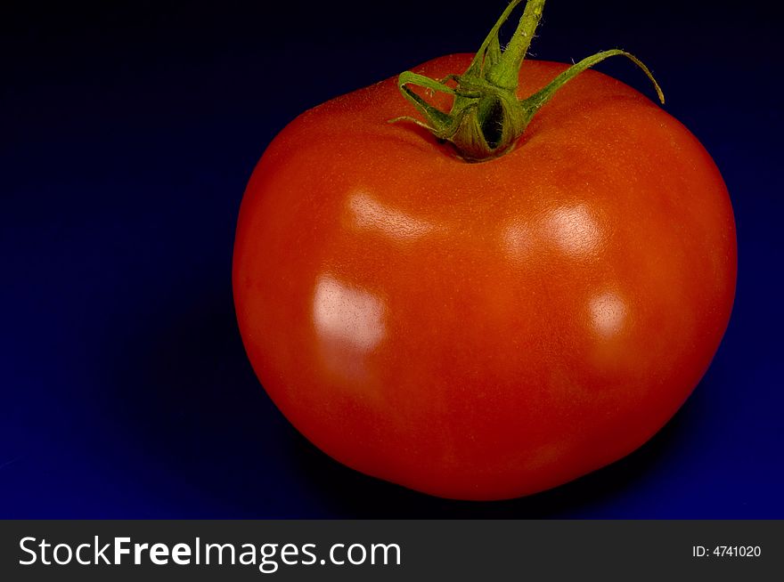 Big red tomato on blue with dark background