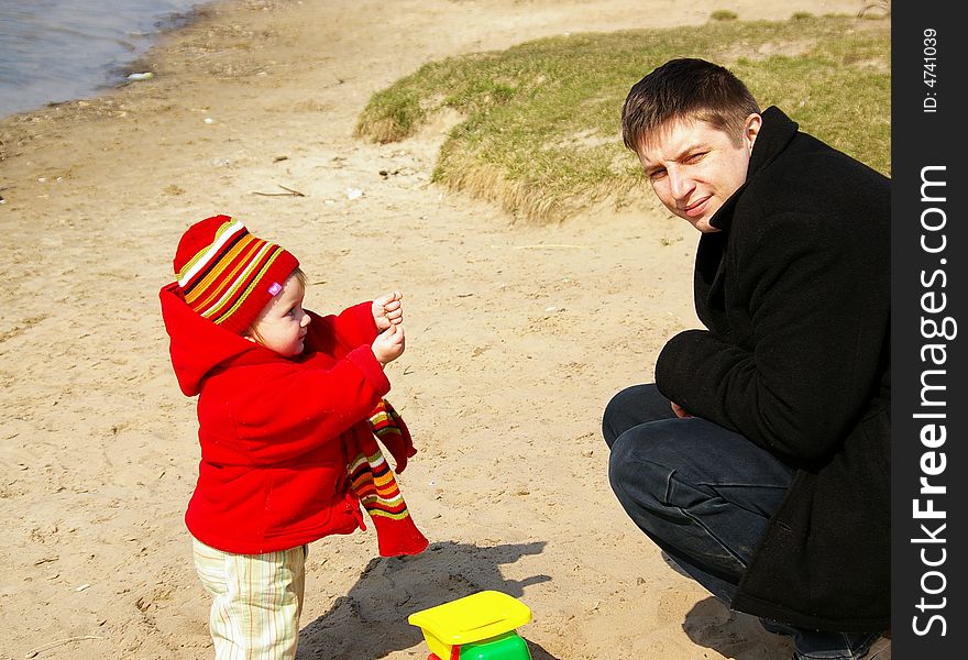 Daddy with a daughter play with sand on coast of lake