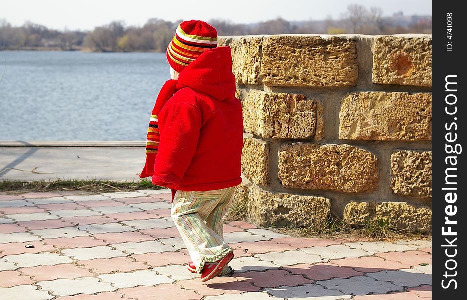 Little girl in a red jacket approaches to lake. Little girl in a red jacket approaches to lake