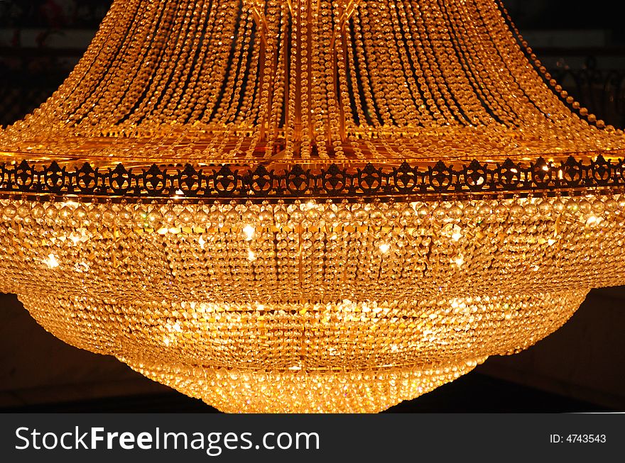 A shiny golden pendant lamp consisting of numerous glass beads and little lights.