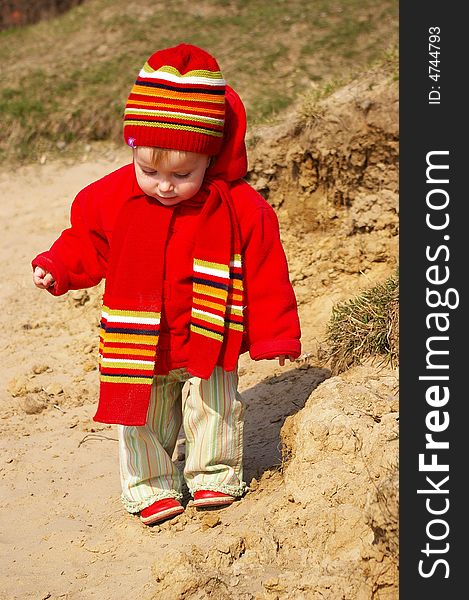 Little girl in the bright cap and  scarf play with sand