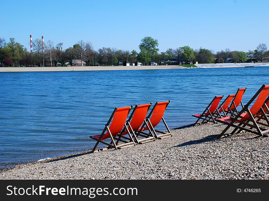 Empty orange folding chairs by blue lake. Empty orange folding chairs by blue lake