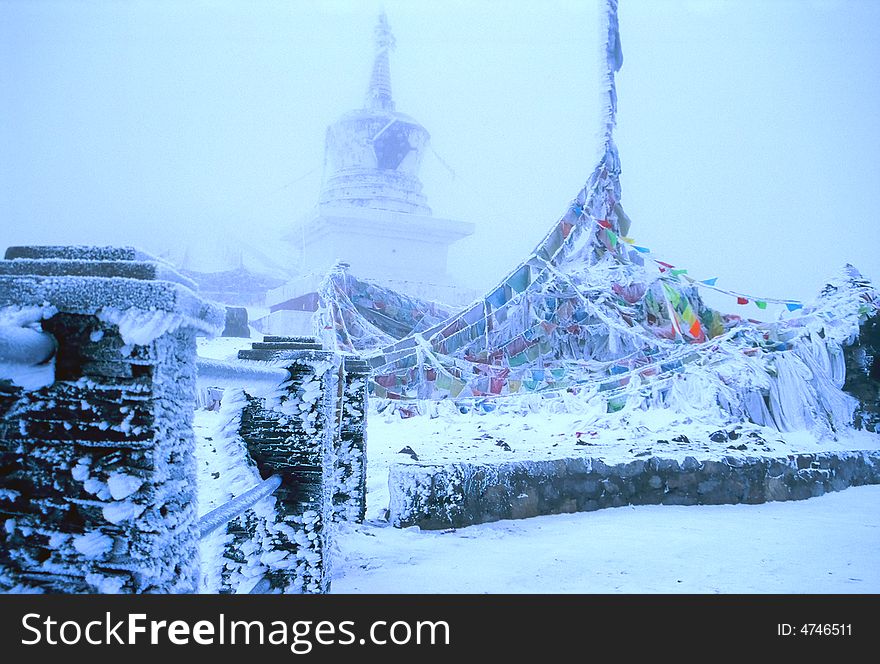 This is a tibetan buddha tower and flags on top of a Tibet moutain, covered with white snow and fog.