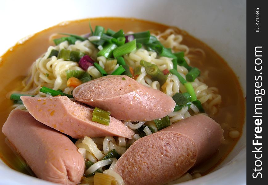 A bowl of instant noodles with spring onion and sausage