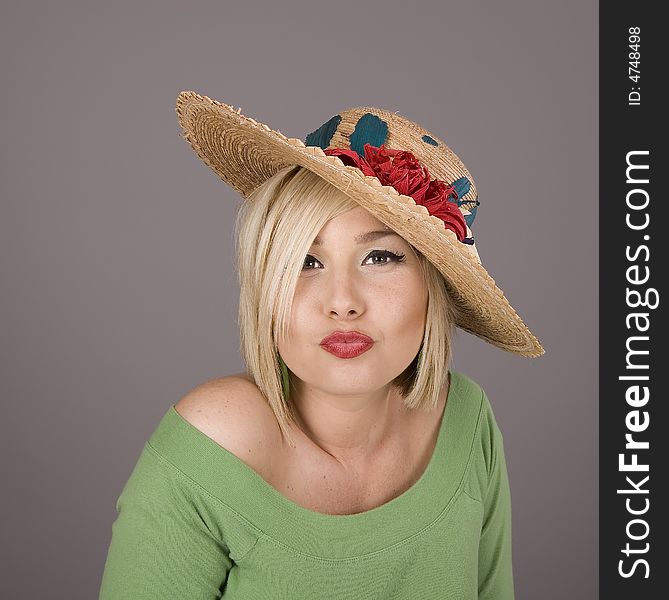 A blonde in a green blouse and a flowered straw hat with lips puckered in a kiss. A blonde in a green blouse and a flowered straw hat with lips puckered in a kiss